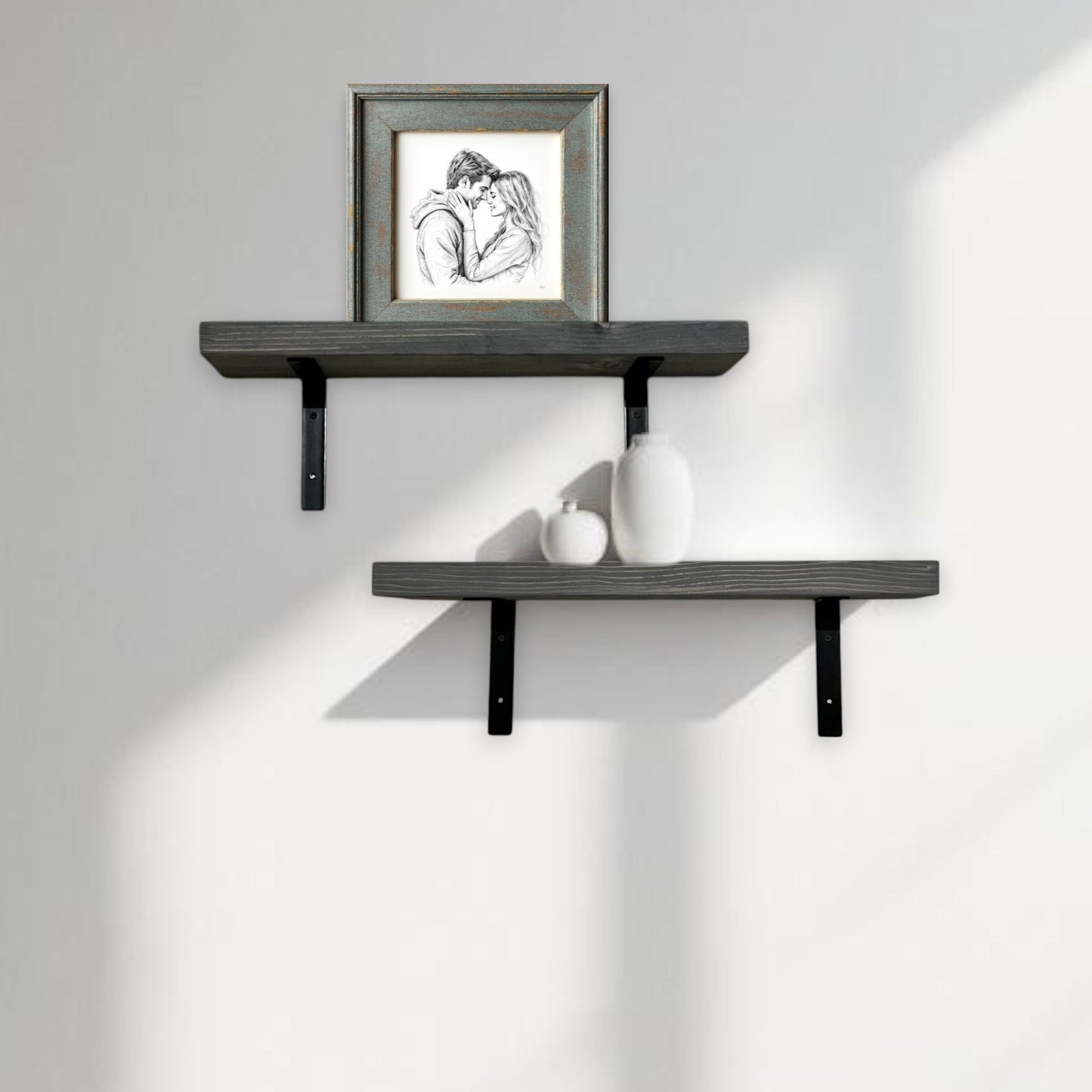 Two dark gray wall shelves with a framed picture and small decorative items on a light gray wall.