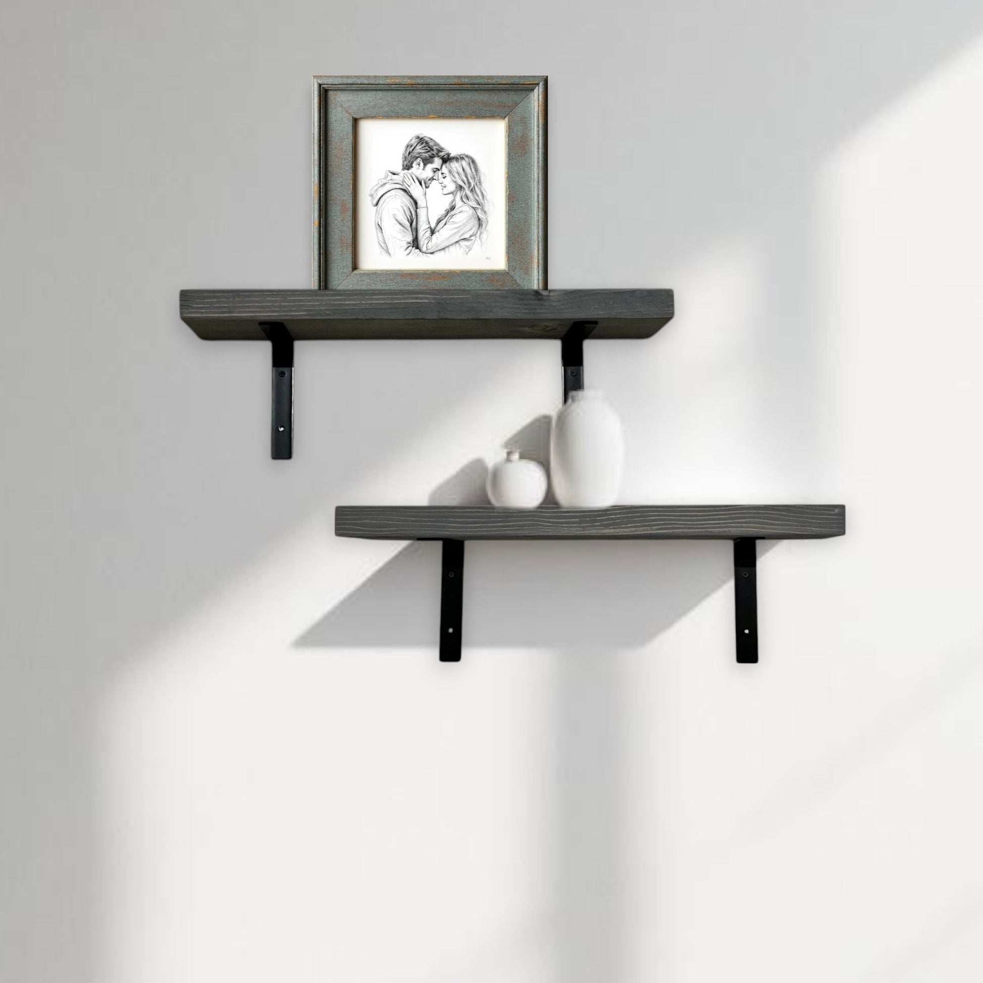 Two dark gray wall shelves with a framed picture and small decorative items on a light gray wall.