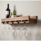 Wooden wall-mounted wine rack with hanging glasses against a plain wall.